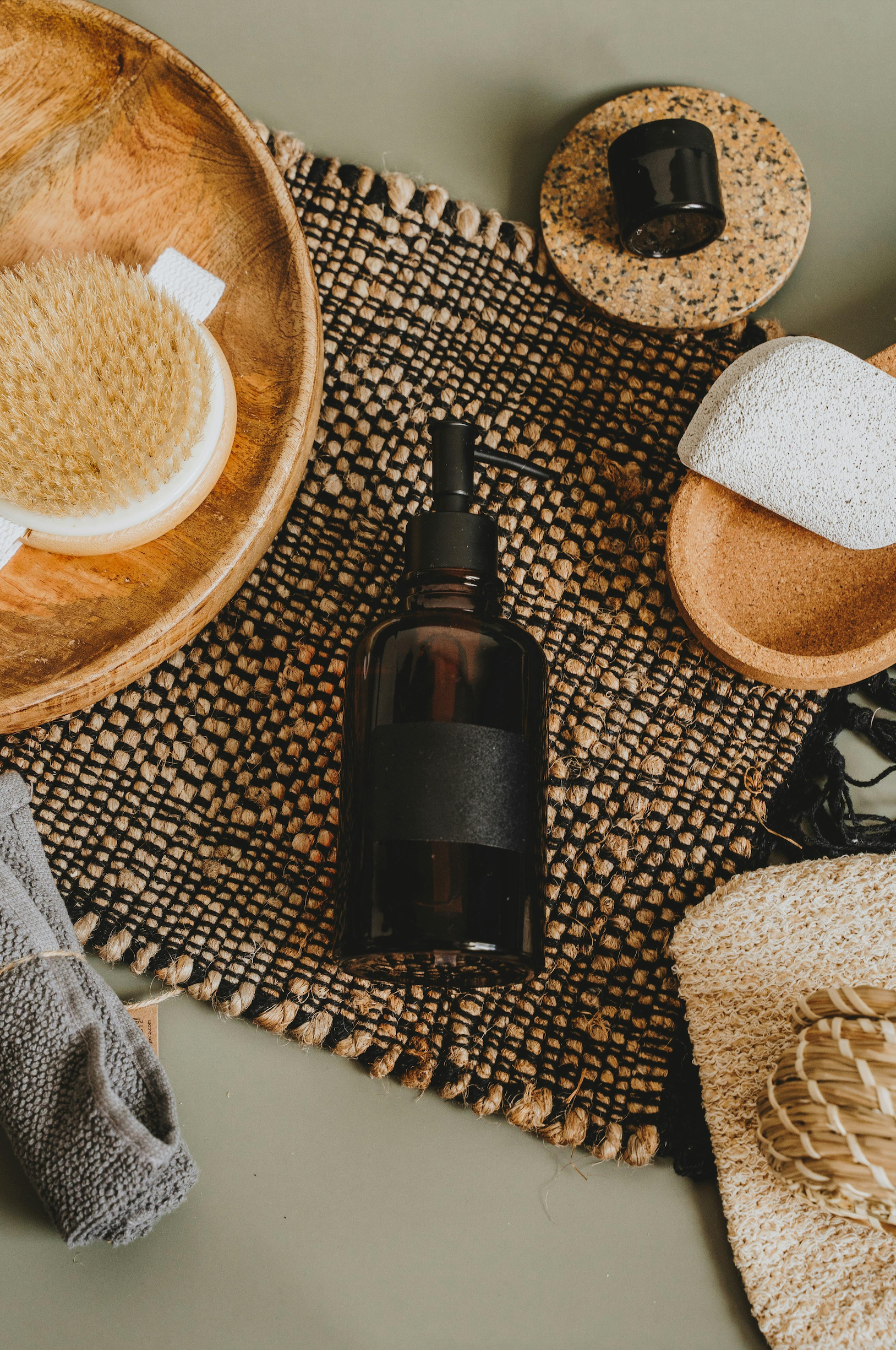 Eco-friendly body care essentials including an amber glass bottle, natural body brush, and soft towel arranged on a clean surface.