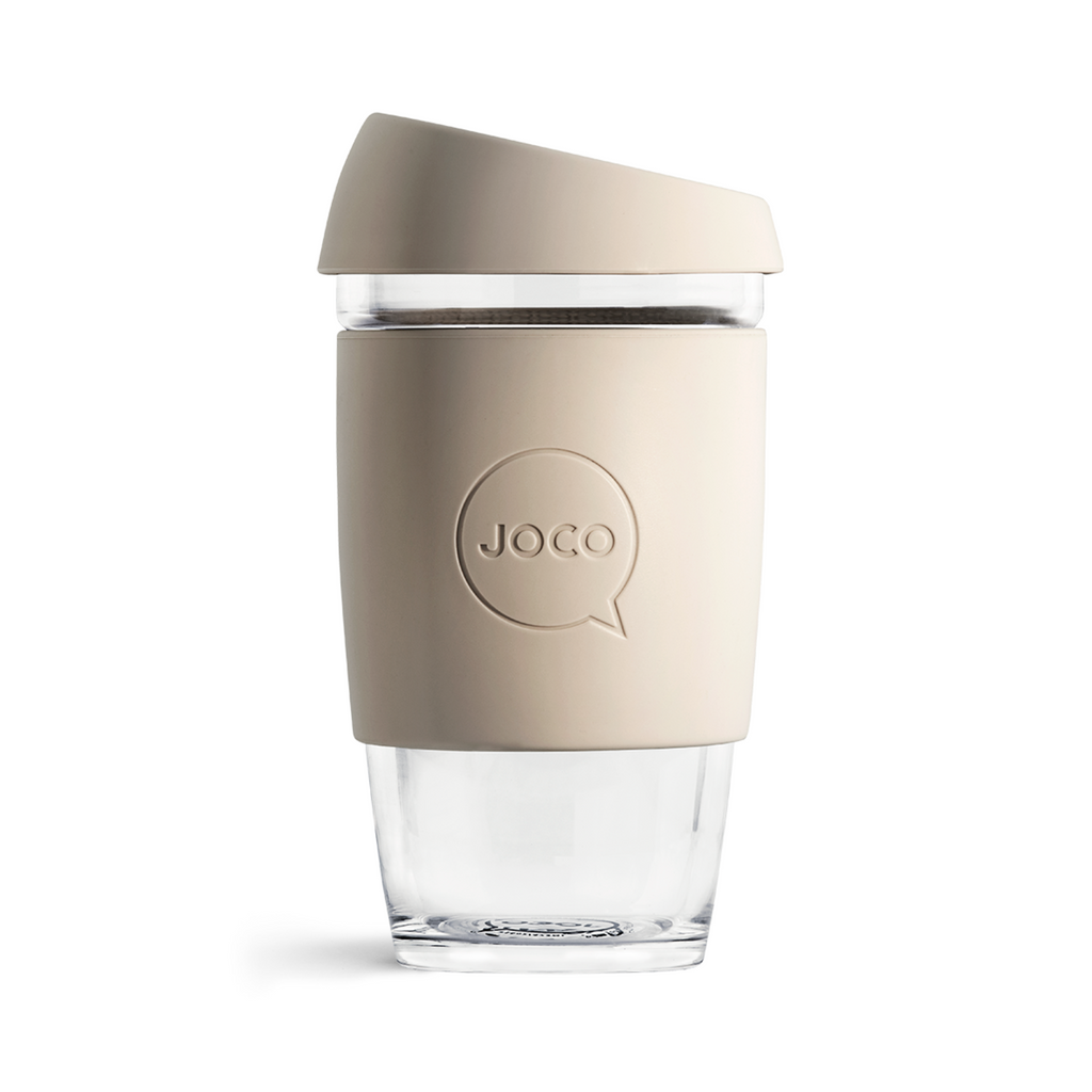 Clear glass reusable coffee cup with beige silicone sleeve on a white background
