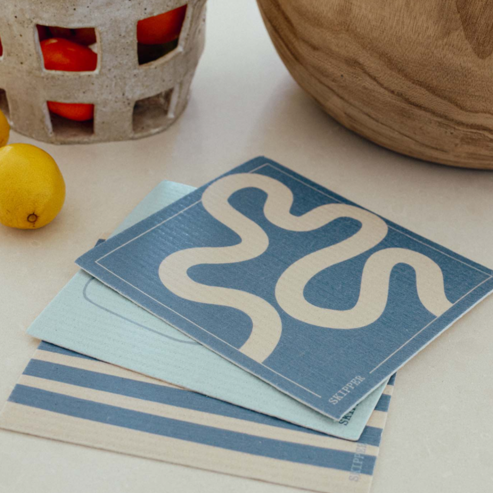 Stack of blue and beige dish cloths with a wavy line design on a light surface.